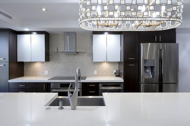 kitchen with stainless steel appliances, wall chimney range hood, light countertops, a sink, and backsplash