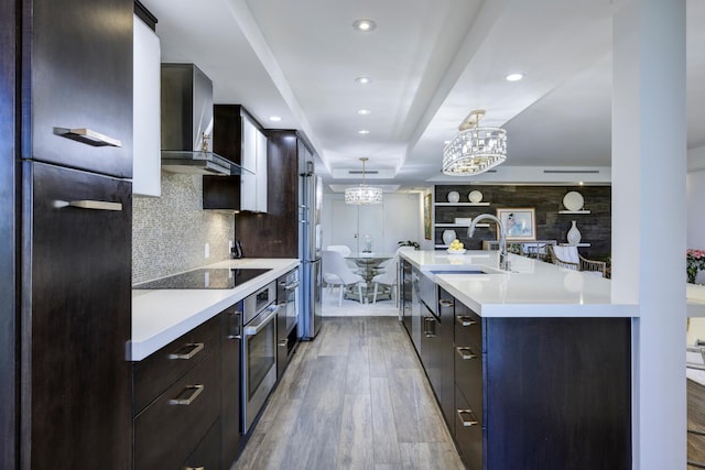 kitchen featuring wall chimney range hood, stainless steel appliances, modern cabinets, light countertops, and a sink