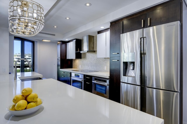 kitchen with appliances with stainless steel finishes, wall chimney exhaust hood, light countertops, a sink, and backsplash