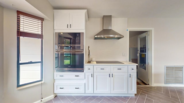 kitchen with white cabinetry, black appliances, and wall chimney range hood