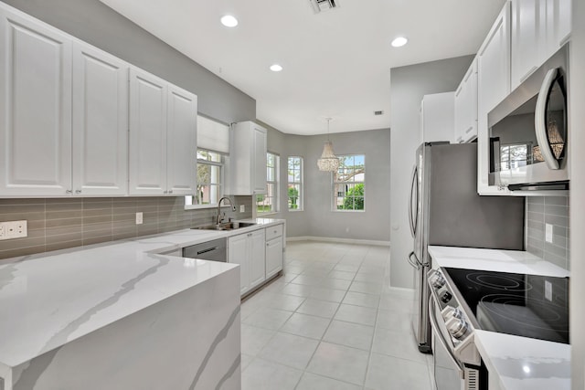 kitchen featuring light stone counters, a sink, white cabinets, appliances with stainless steel finishes, and decorative light fixtures