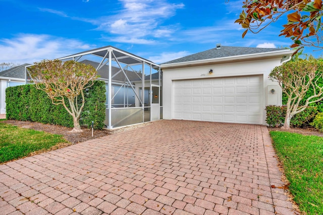 view of front facade with decorative driveway, glass enclosure, an attached garage, and stucco siding