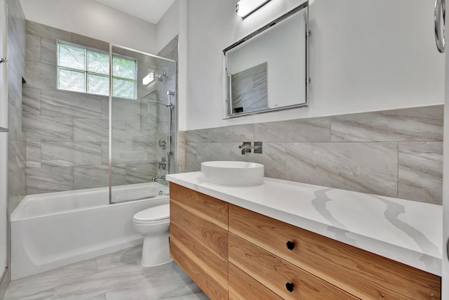 full bath with toilet, tile walls, vanity, wainscoting, and shower / bath combination with glass door