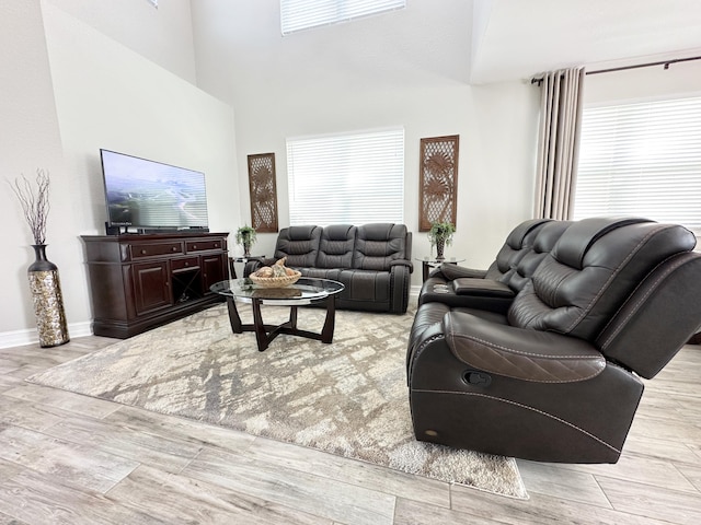 living room with a towering ceiling, light wood-style flooring, and baseboards