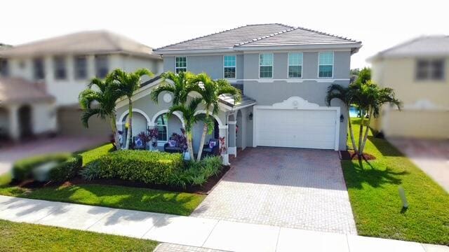 view of front of property featuring a garage, stucco siding, decorative driveway, and a front yard