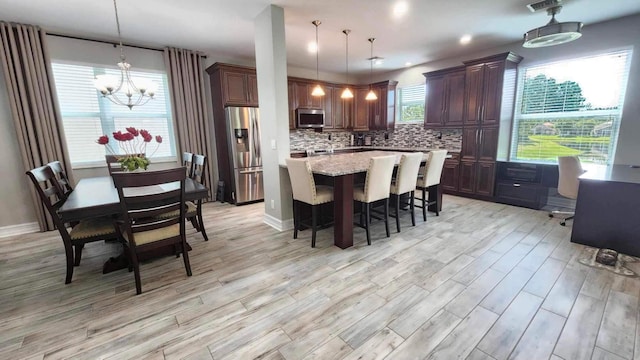 kitchen featuring decorative light fixtures, a kitchen island, light stone counters, appliances with stainless steel finishes, and decorative backsplash