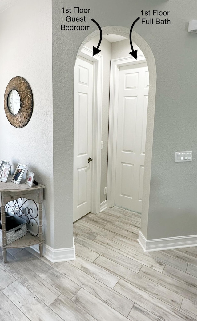 corridor featuring arched walkways, a textured wall, wood finish floors, and baseboards