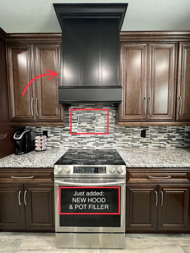 kitchen with light stone counters, decorative backsplash, dark brown cabinetry, premium range hood, and stainless steel electric range