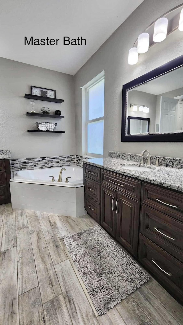 bathroom featuring wood finished floors, vanity, and a bath