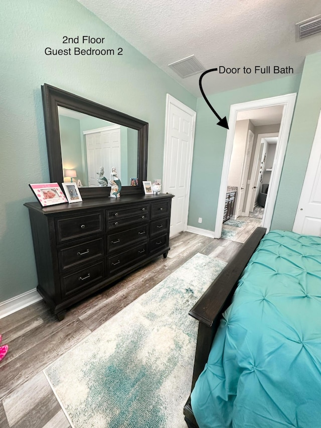 bedroom with light wood-style floors, visible vents, a textured ceiling, and baseboards