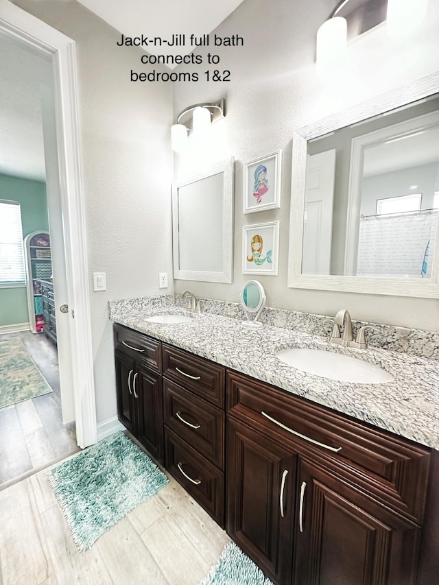 full bathroom with double vanity, baseboards, a sink, and wood finished floors