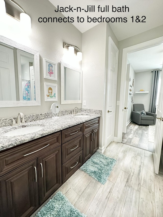 full bathroom featuring double vanity, wood finished floors, a sink, and baseboards