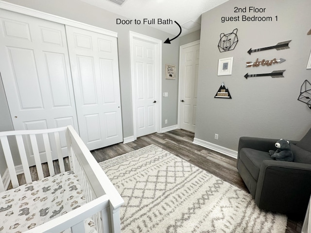 bedroom with dark wood-type flooring, a closet, a crib, and baseboards