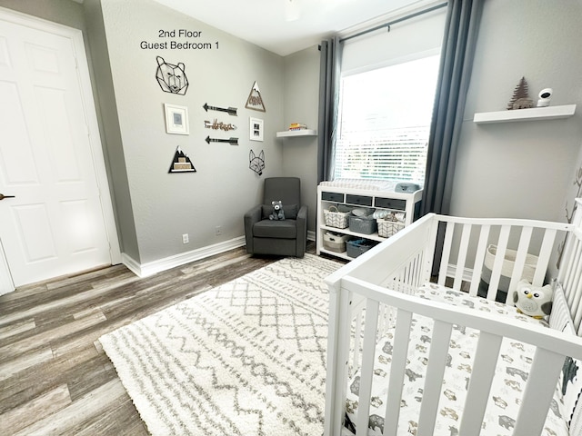 bedroom featuring a crib, baseboards, and wood finished floors