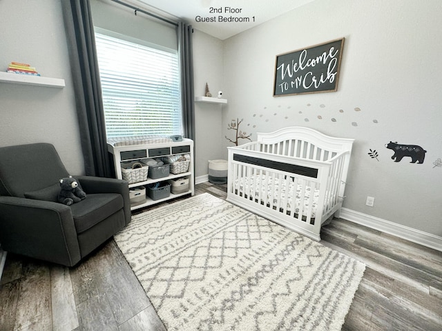 bedroom featuring a nursery area, dark wood-type flooring, and baseboards