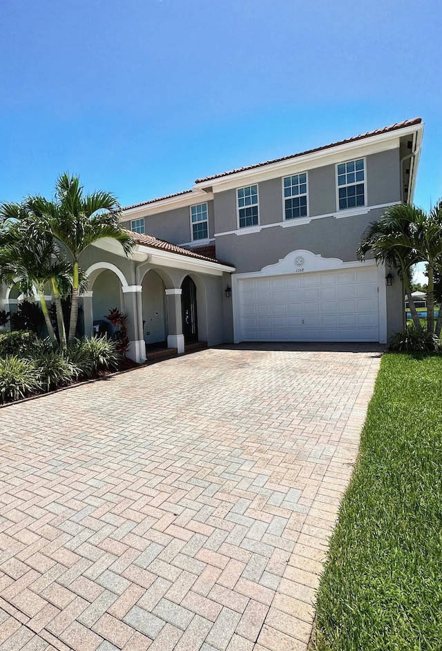 view of front facade with decorative driveway, an attached garage, a tile roof, and stucco siding