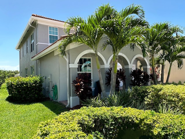 view of side of home featuring a yard, a tiled roof, and stucco siding