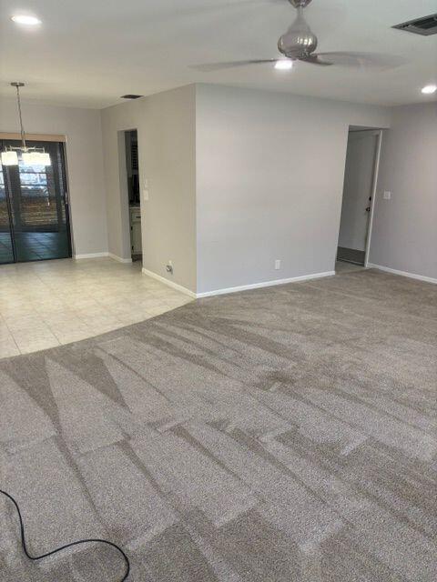 spare room with light colored carpet, ceiling fan, visible vents, and baseboards