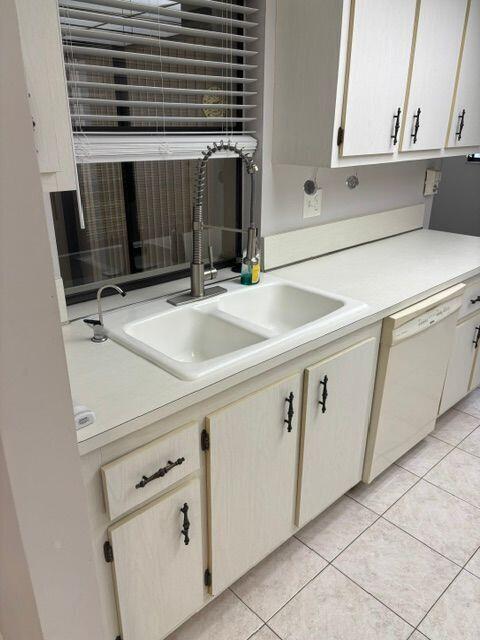 kitchen with light tile patterned floors, light countertops, white dishwasher, and a sink