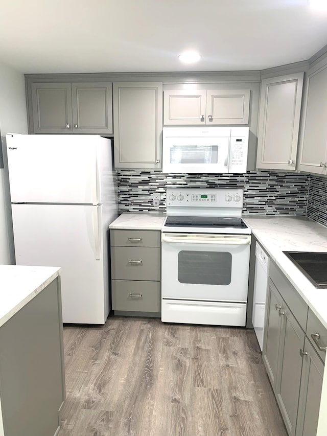 kitchen with wood finished floors, white appliances, gray cabinets, and decorative backsplash