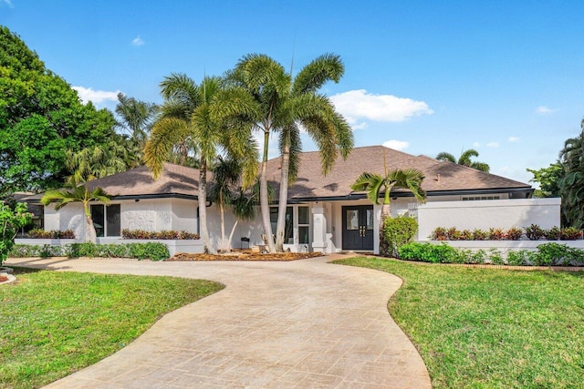 view of front of property featuring stucco siding, a front yard, decorative driveway, and fence