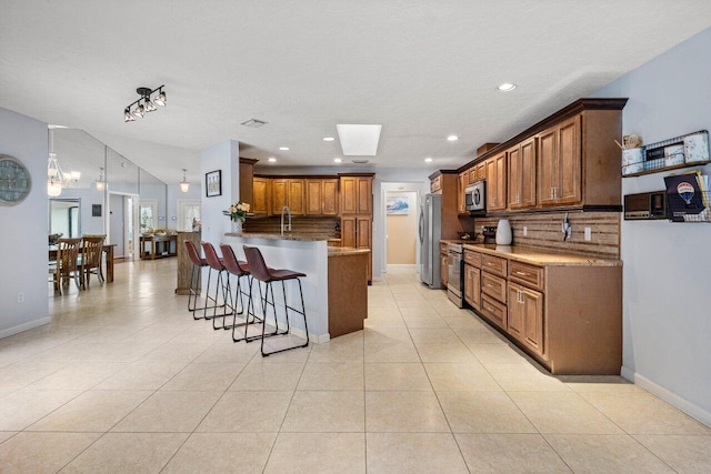 kitchen with a breakfast bar area, appliances with stainless steel finishes, brown cabinetry, backsplash, and a peninsula