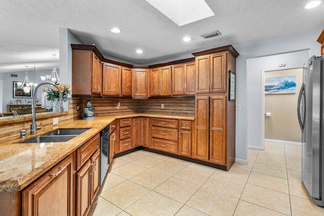 kitchen featuring freestanding refrigerator, a sink, a peninsula, brown cabinets, and pendant lighting