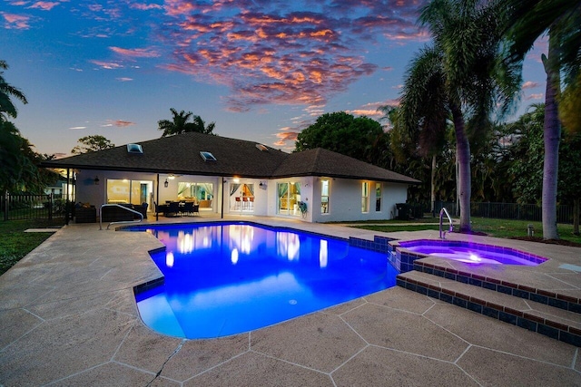 pool at dusk featuring a pool with connected hot tub, a patio area, and fence