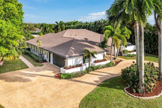 view of front of home with a garage, roof with shingles, central air condition unit, a front lawn, and decorative driveway