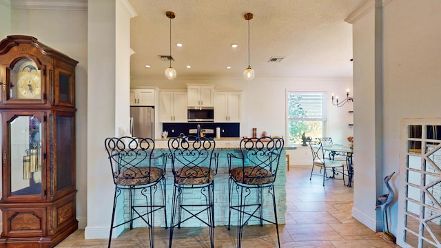 kitchen with hanging light fixtures, a kitchen breakfast bar, stainless steel appliances, white cabinets, and crown molding