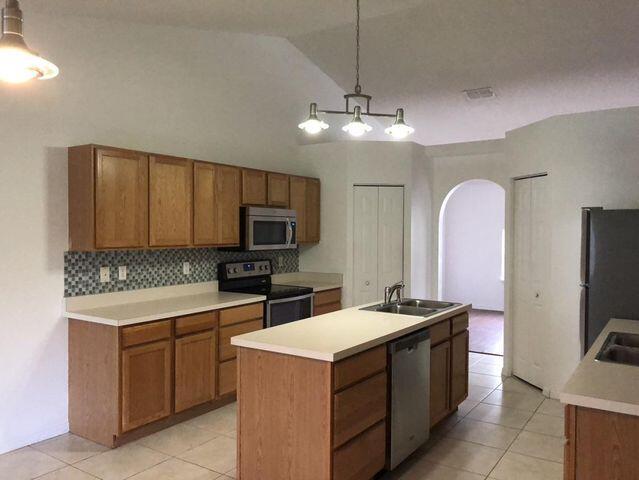 kitchen with appliances with stainless steel finishes, sink, backsplash, pendant lighting, and a kitchen island with sink