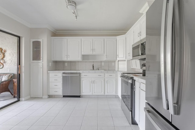 kitchen with appliances with stainless steel finishes, light tile patterned floors, ornamental molding, and white cabinets