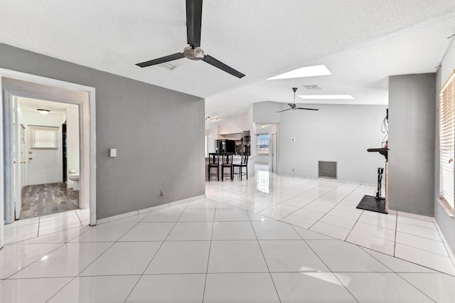 unfurnished living room with light tile patterned floors, vaulted ceiling with skylight, a textured ceiling, visible vents, and a ceiling fan