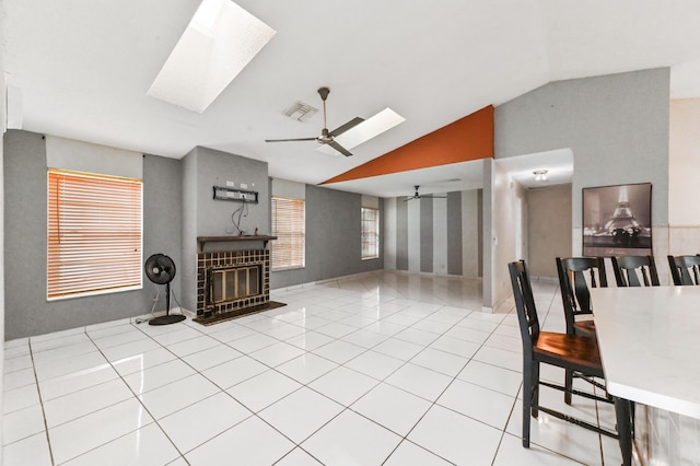 tiled living area with ceiling fan, vaulted ceiling with skylight, a glass covered fireplace, and visible vents