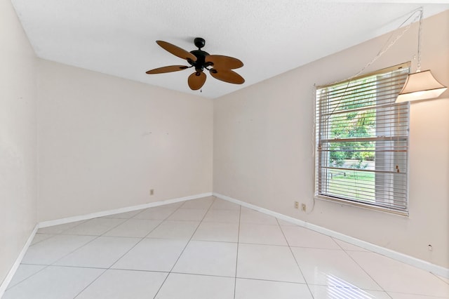 empty room featuring light tile patterned floors, ceiling fan, baseboards, and a textured ceiling