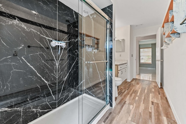 full bathroom with a marble finish shower, baseboards, toilet, wood finished floors, and vanity