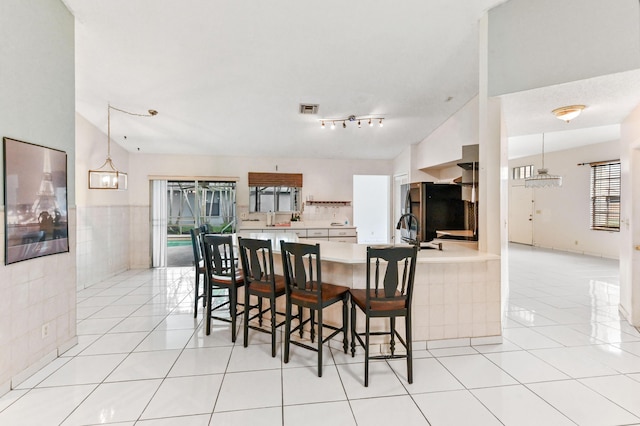 kitchen with light tile patterned floors, a peninsula, visible vents, light countertops, and freestanding refrigerator