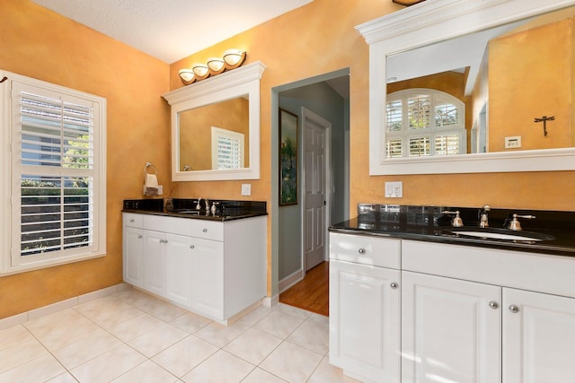 full bath featuring a wealth of natural light, tile patterned flooring, two vanities, and a sink