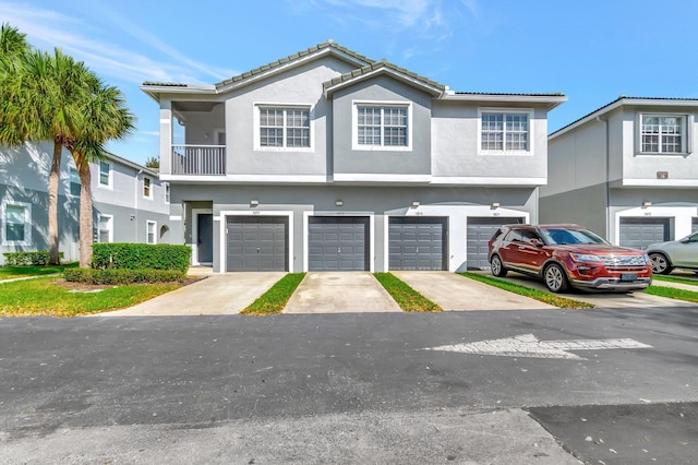 multi unit property with a balcony, driveway, a tile roof, stucco siding, and an attached garage