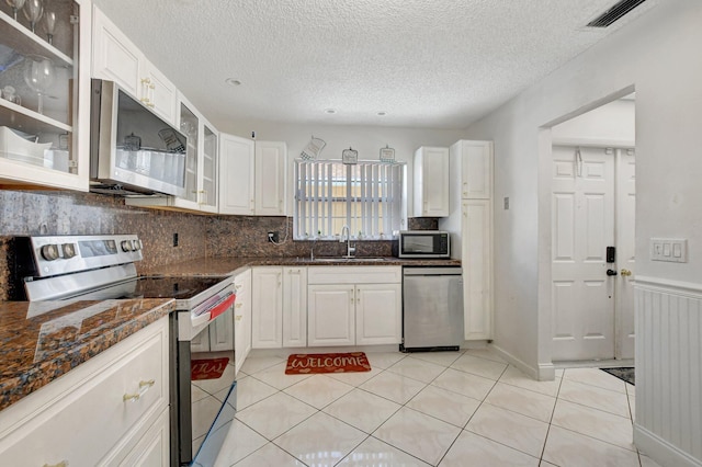 kitchen featuring stainless steel appliances, a sink, visible vents, white cabinetry, and glass insert cabinets