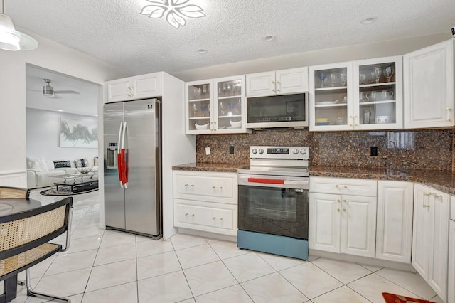 kitchen featuring stainless steel appliances, decorative backsplash, glass insert cabinets, white cabinets, and dark stone counters