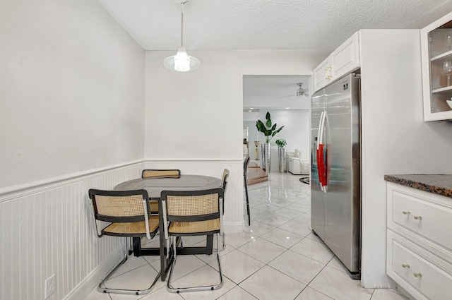 dining space with a wainscoted wall, a textured ceiling, and light tile patterned flooring