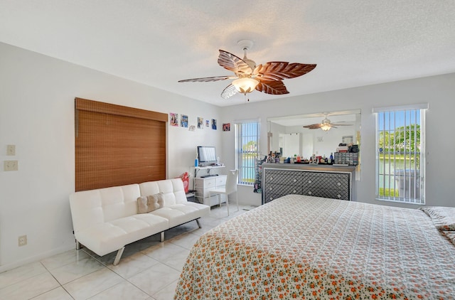 bedroom with ceiling fan, baseboards, a textured ceiling, and light tile patterned flooring