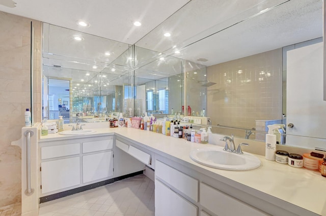 bathroom with double vanity, tiled shower, a sink, and recessed lighting