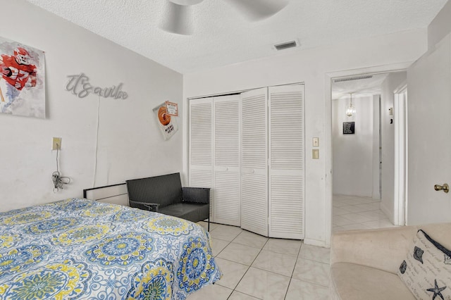 bedroom with light tile patterned floors, visible vents, a ceiling fan, a textured ceiling, and a closet