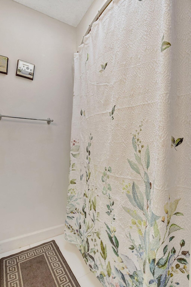 bathroom with a textured ceiling, tile patterned flooring, and baseboards