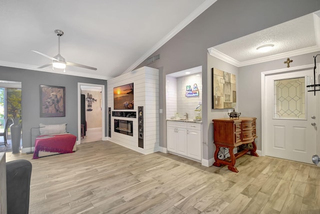 interior space with lofted ceiling, visible vents, light wood-style floors, a glass covered fireplace, and crown molding