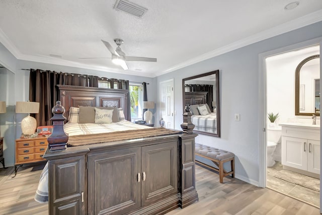 bedroom with light wood finished floors, baseboards, visible vents, ornamental molding, and ensuite bathroom