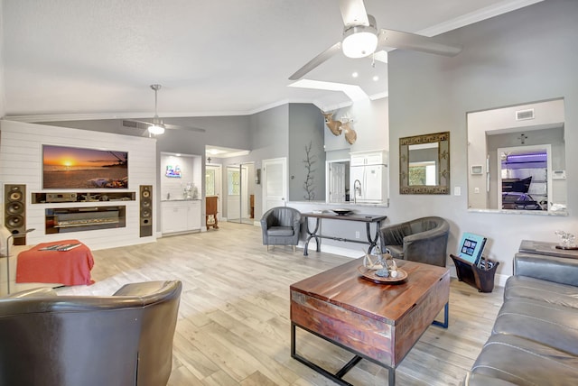 living area with crown molding, light wood finished floors, visible vents, a glass covered fireplace, and ceiling fan