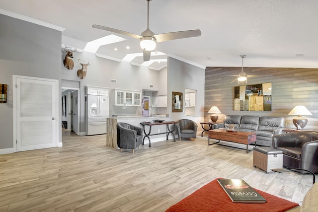 living area featuring ceiling fan, high vaulted ceiling, a skylight, light wood-style floors, and ornamental molding